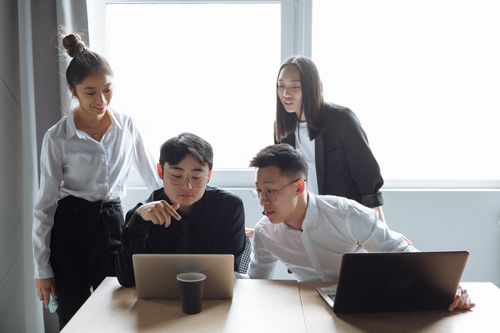 Free Four young professionals engaged in a collaborative meeting in an office setting with laptops. Stock Photo