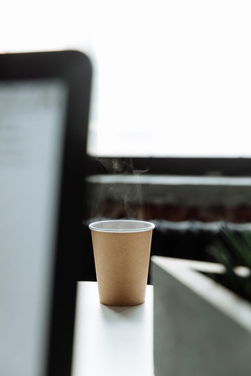Free A minimalist shot of a steaming coffee cup beside a laptop in a bright office space. Stock Photo