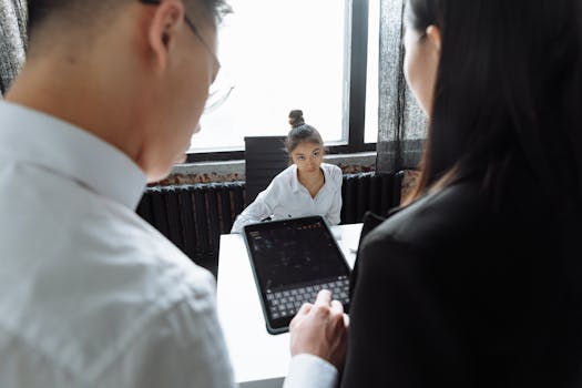 Professionals discussing project around a table using a tablet, in a modern office setting.