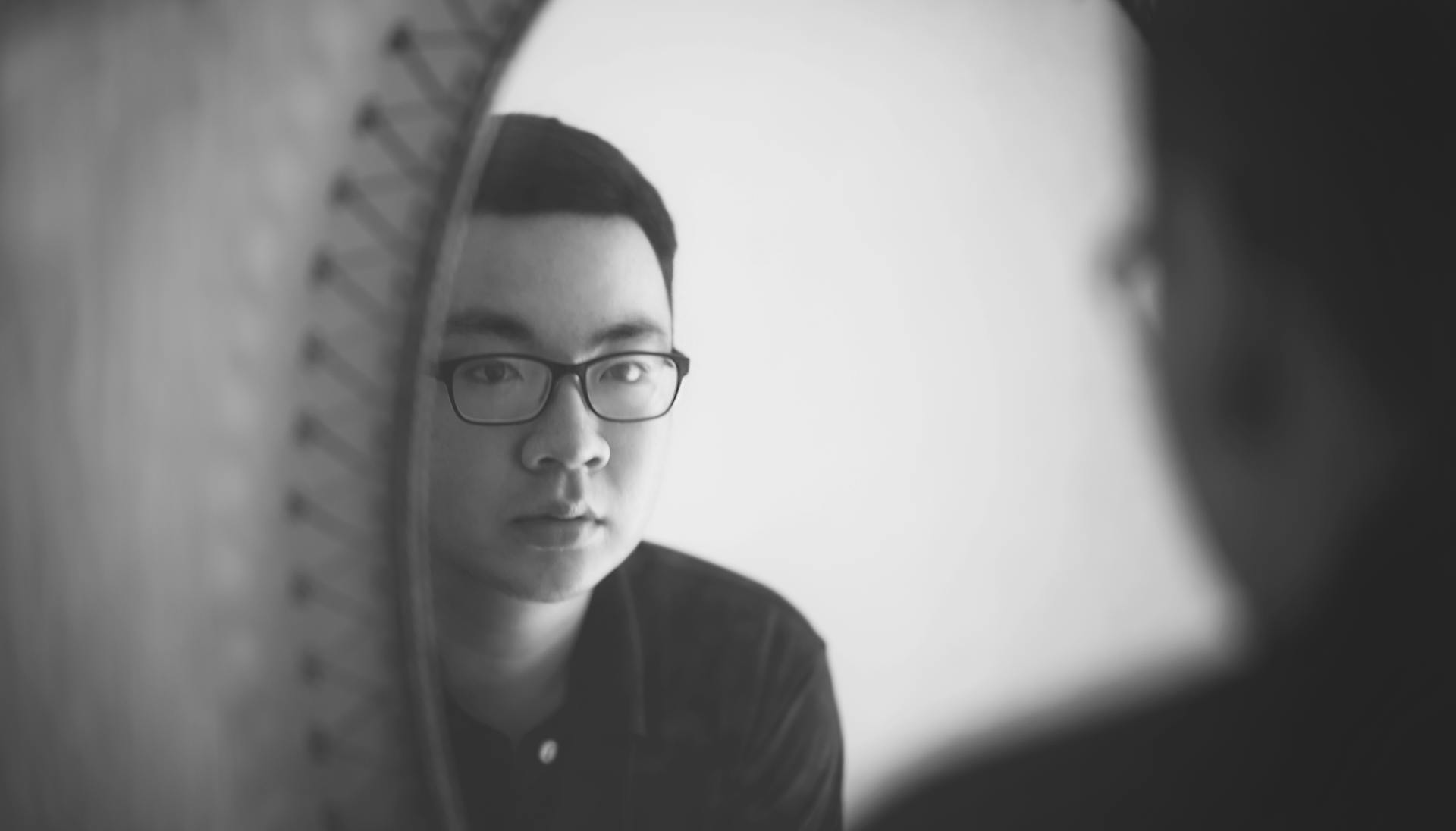 Monochrome portrait of a man looking at his reflection in a mirror.