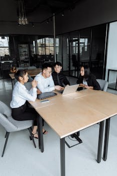 Business professionals engaged in a collaborative discussion around a conference table in a modern office setting.