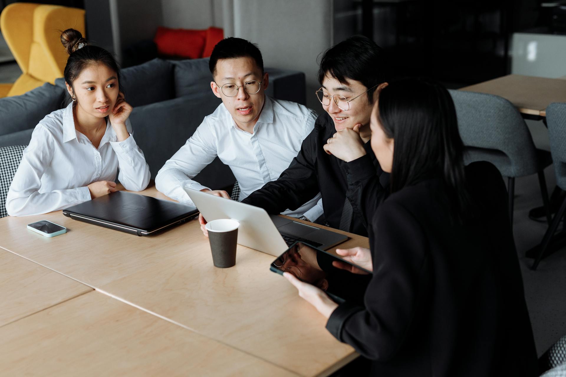 A group of colleagues engaged in a business meeting discussing plans around a laptop in a modern office.