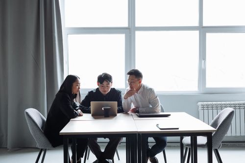Free Three professionals collaborating around a laptop in a bright, modern office setting. Stock Photo