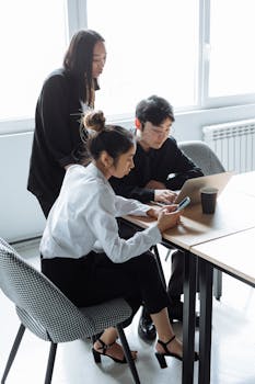 Three colleagues collaborating in a modern office setting with laptops and phones.