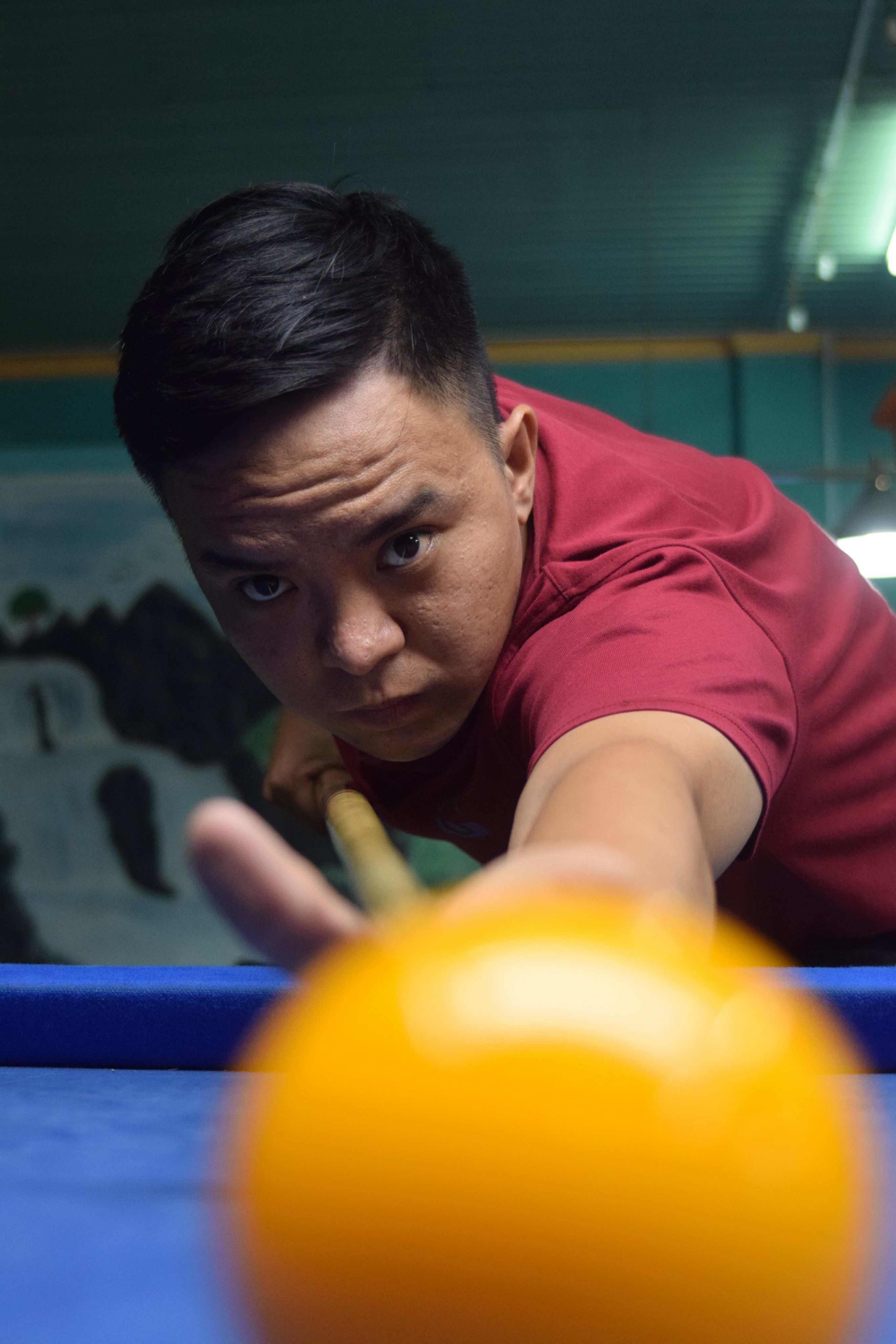 A man intensely concentrating, aiming a billiard cue at a ball on the table.