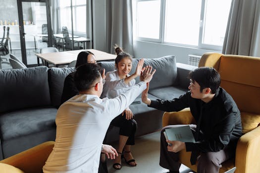 Asian business team discussing and high-fiving in a modern office lounge. Collaborative workplace environment.