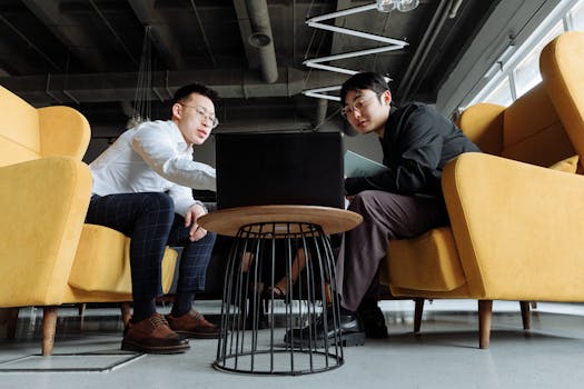 Two men collaborating on a project in a stylish office setting with yellow chairs.