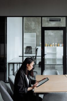 Asian woman focused on using a tablet in a modern office environment.