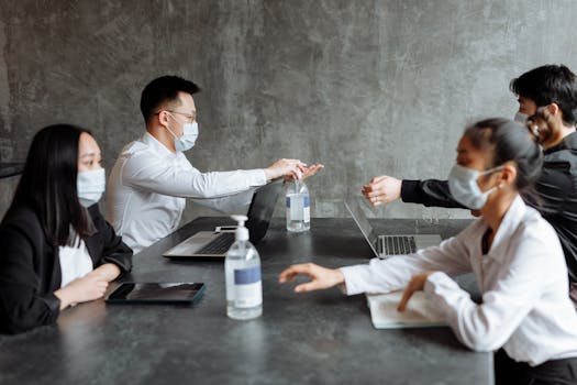 Office colleagues wearing masks practicing hygiene at a meeting with laptops.
