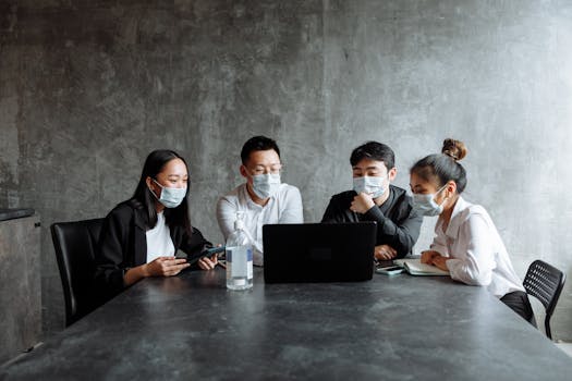 A professional team wearing face masks discusses a project in a modern office setting.
