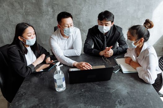 A group of professionals wearing masks during a team meeting, emphasizing workplace safety.