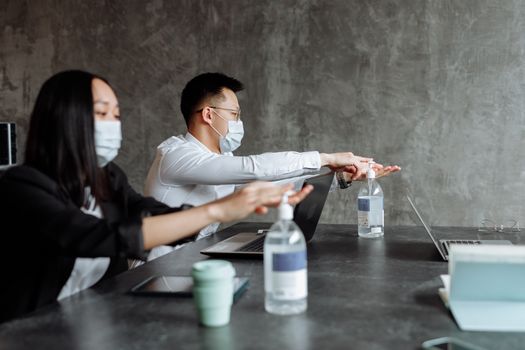 Office workers using sanitizer with masks, emphasizing pandemic safety measures.