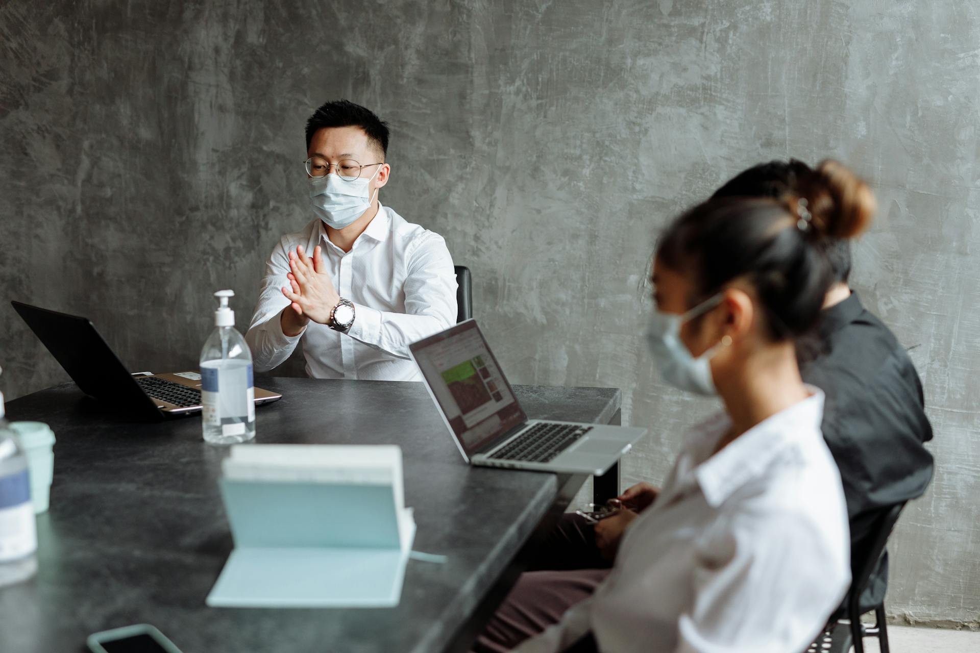 Professionals discussing plans in an office while wearing masks and using laptops.