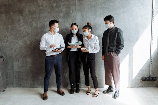 Four coworkers in masks discuss business inside a modern office setting.