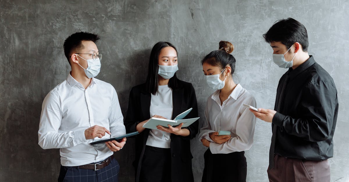 Four professionals wearing face masks collaborate with tablets and notebooks indoors.