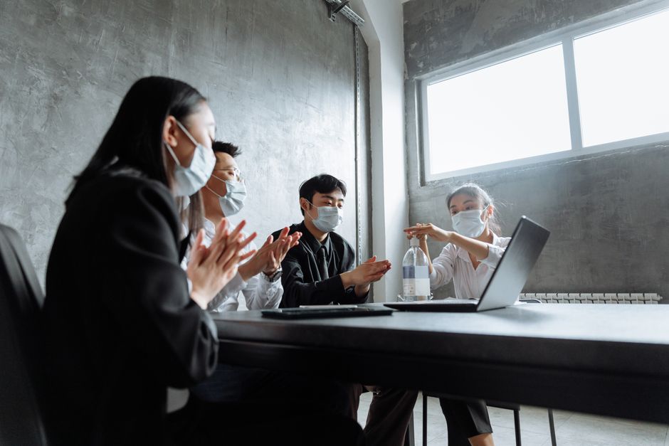 Colegas en un entorno de oficina utilizan desinfectante de manos, usando mascarillas durante una reunión.