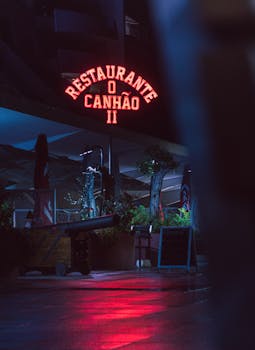 Neon sign of Restaurante O Canhão II glowing at night in Sesimbra, Portugal, creating a vibrant atmosphere.
