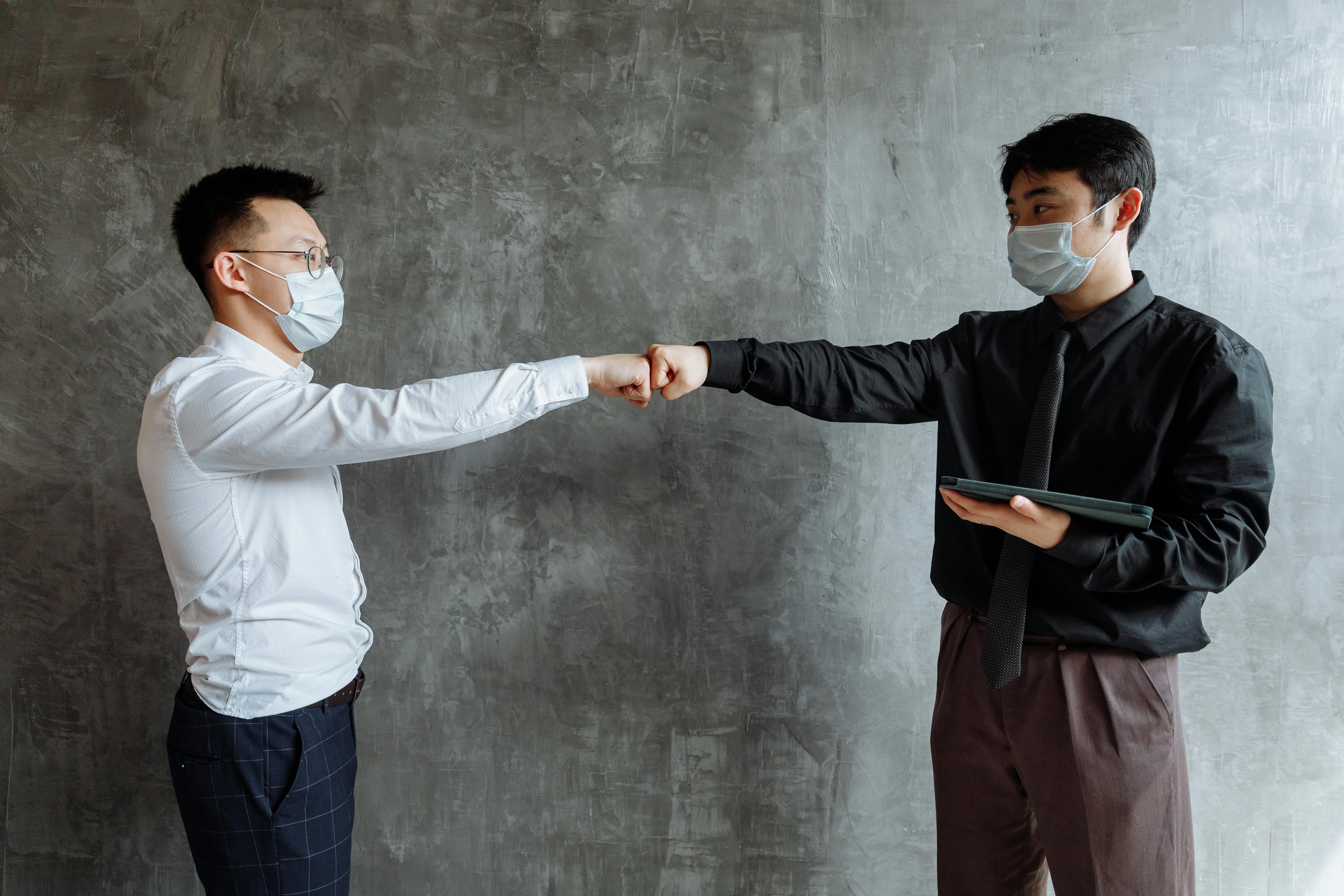 men wearing face masks doing a fist bump