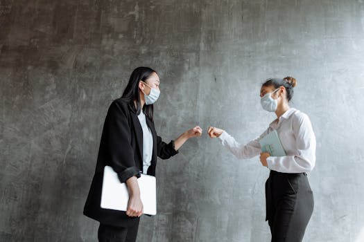 Two professionals wearing masks exchange a fist bump, symbolizing workplace camaraderie.