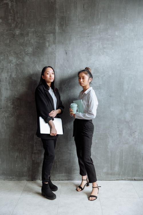 Free Two professional women posing in sleek business attire against a gray wall. Stock Photo