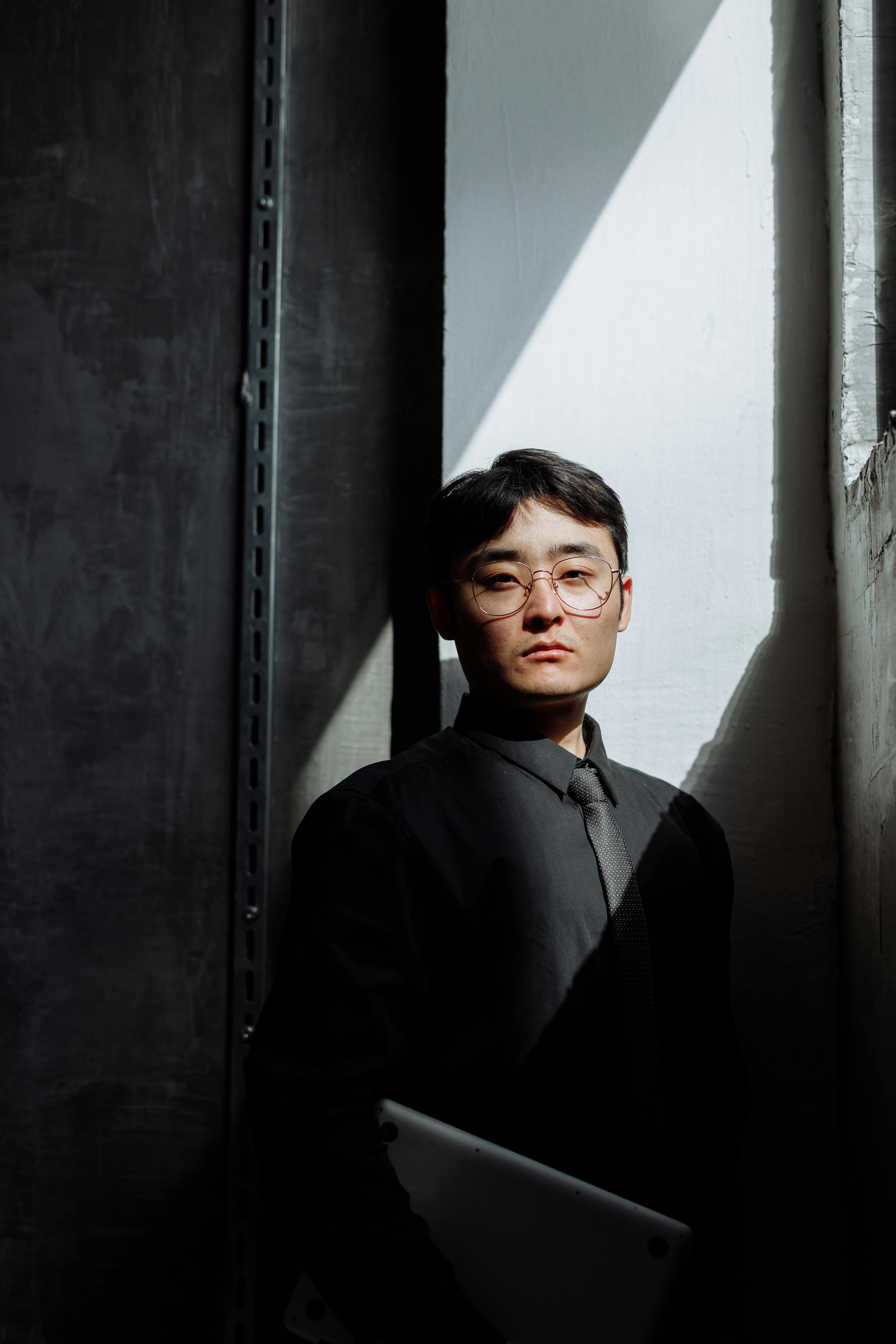 man in black dress shirt standing beside gray wall