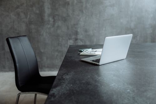 Free A sleek workspace featuring a laptop on a gray table with a leather chair, creating a minimalist office vibe. Stock Photo