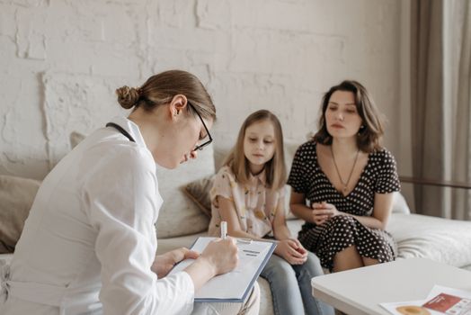 A female doctor consults with a mother and daughter inside a cozy room.