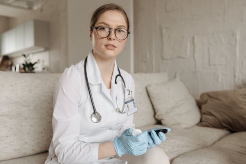 A Doctor with Stethoscope Wearing Blue Gloves Sitting on a Couch while Looking at the Camera