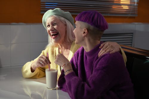 Woman in Purple Sweater Sitting Beside an Elderly Woman in Yellow Sweater while Having a Conversation