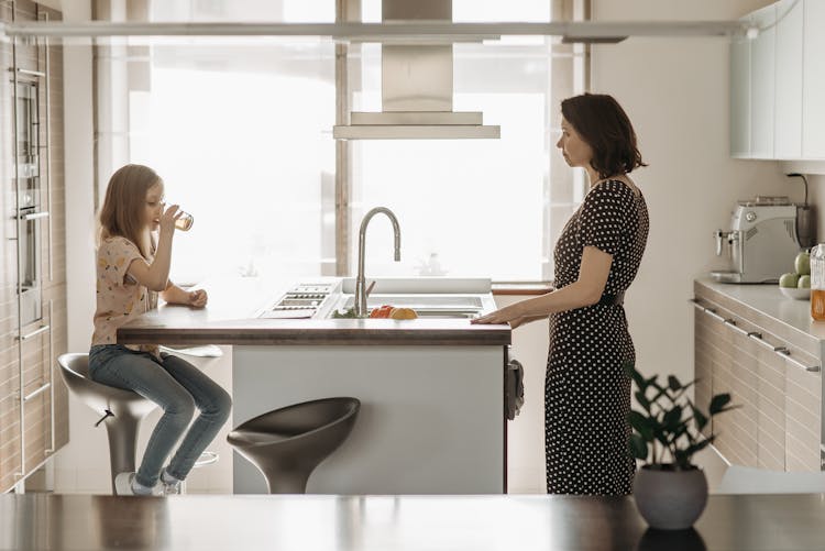 A Woman Looking At Her Daughter Drinking Juice