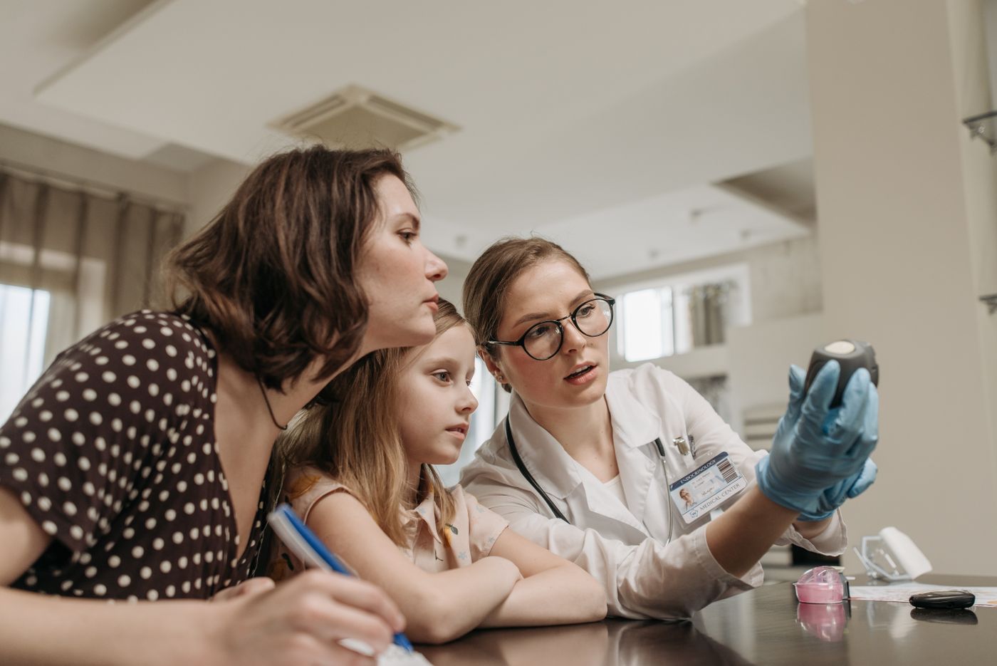 A clinician showing a mother and child how to use a blood glucose meter