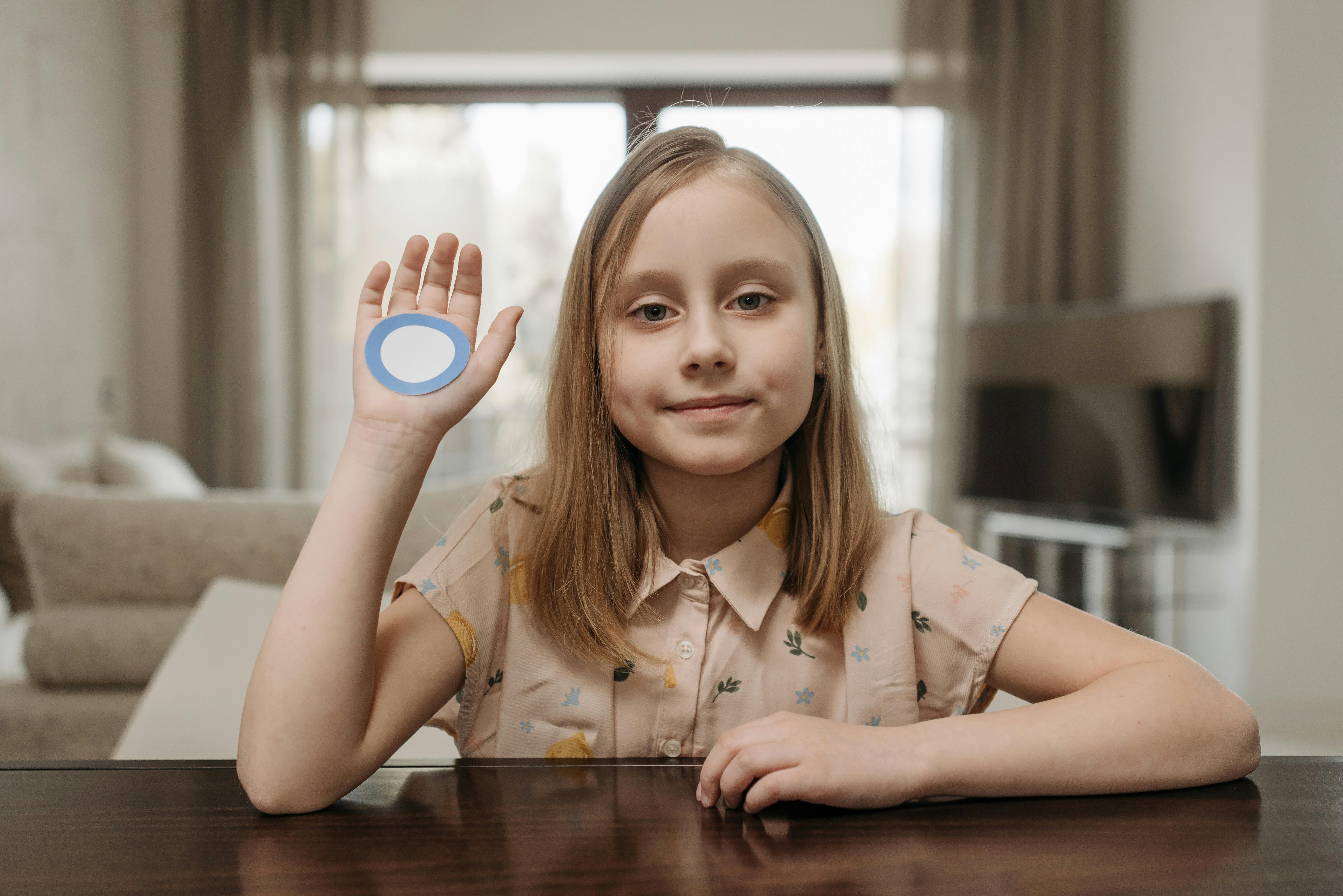 Young girl sitting indoors, raising hand with blue diabetes awareness circle symbol.