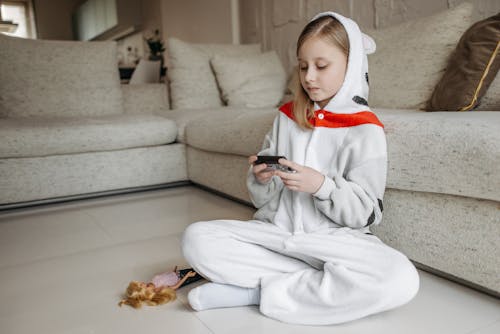 Girl in a Costume Sitting on the Floor by the Sofa and Holding Her Glucometer 