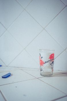 A glass with floral design on a white tiled counter and a blue utility knife nearby.