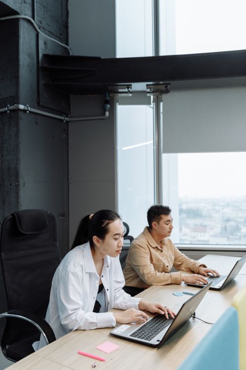 Free Two professionals working collaboratively in a modern office setting with laptops. Stock Photo