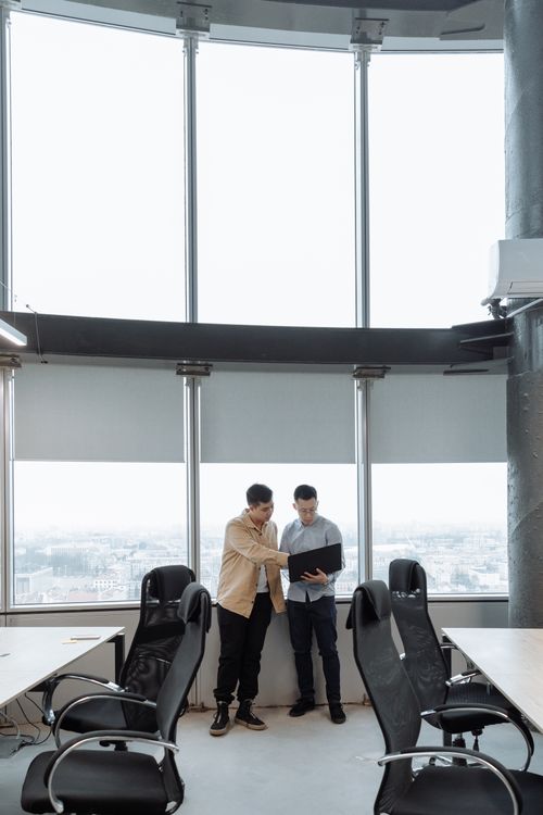 Free Two men collaborating in a modern office setting with large windows. Stock Photo