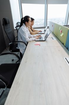 Two professionals working on laptops in a modern office setup, focused on teamwork.