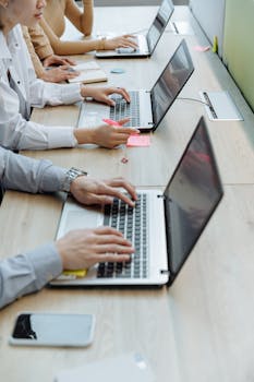 Group of office workers typing on laptops at a shared workspace desk.