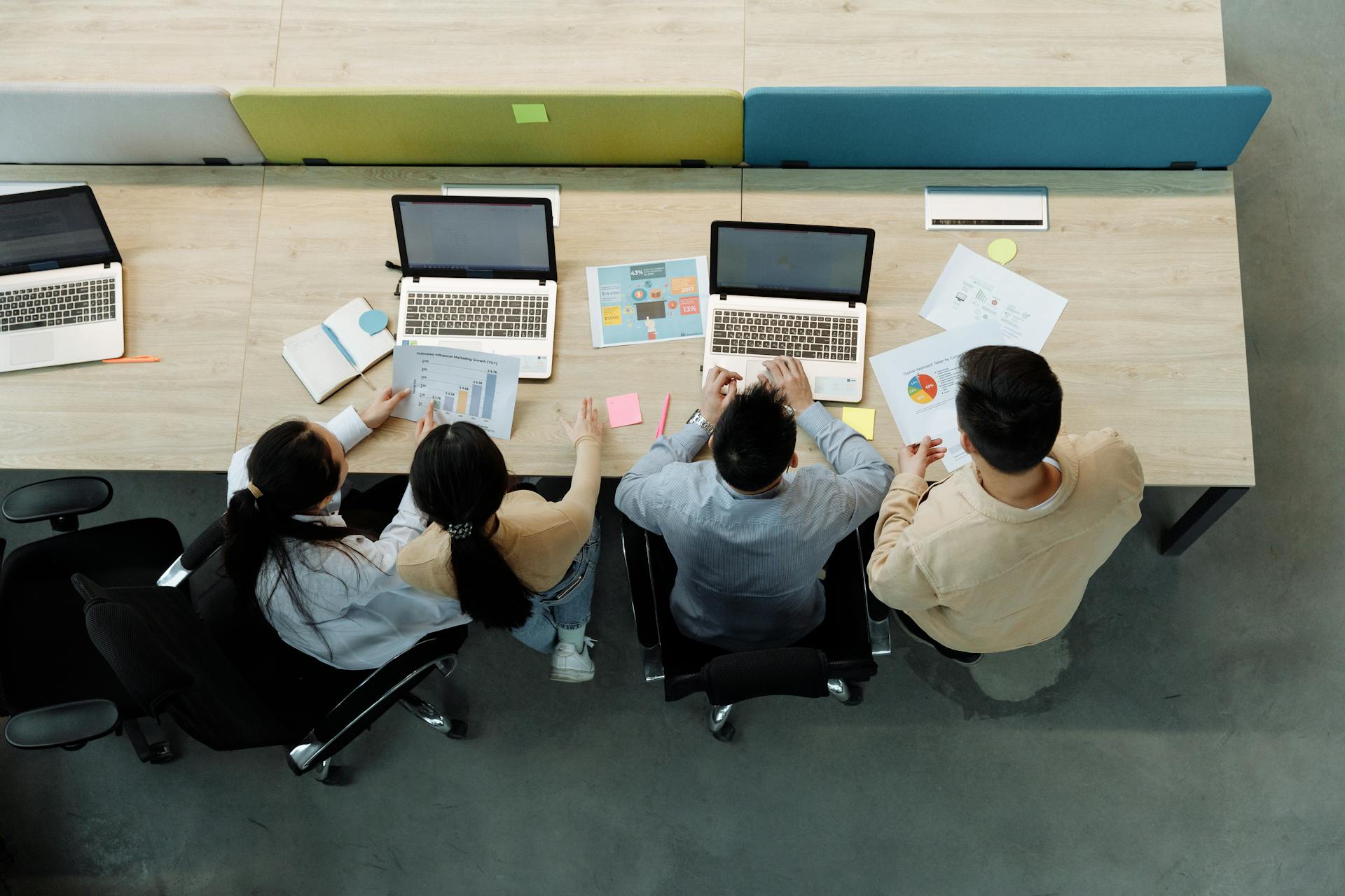 Aerial view of four colleagues working with laptops and documents at a shared desk.