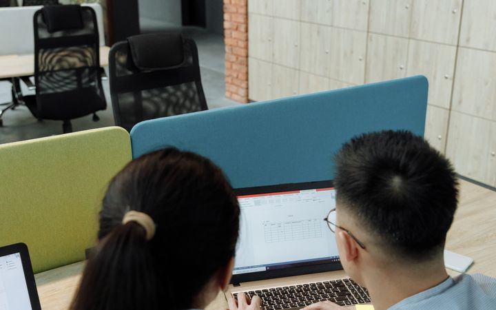 Two colleagues collaborating on a laptop in a modern, open-plan office space.