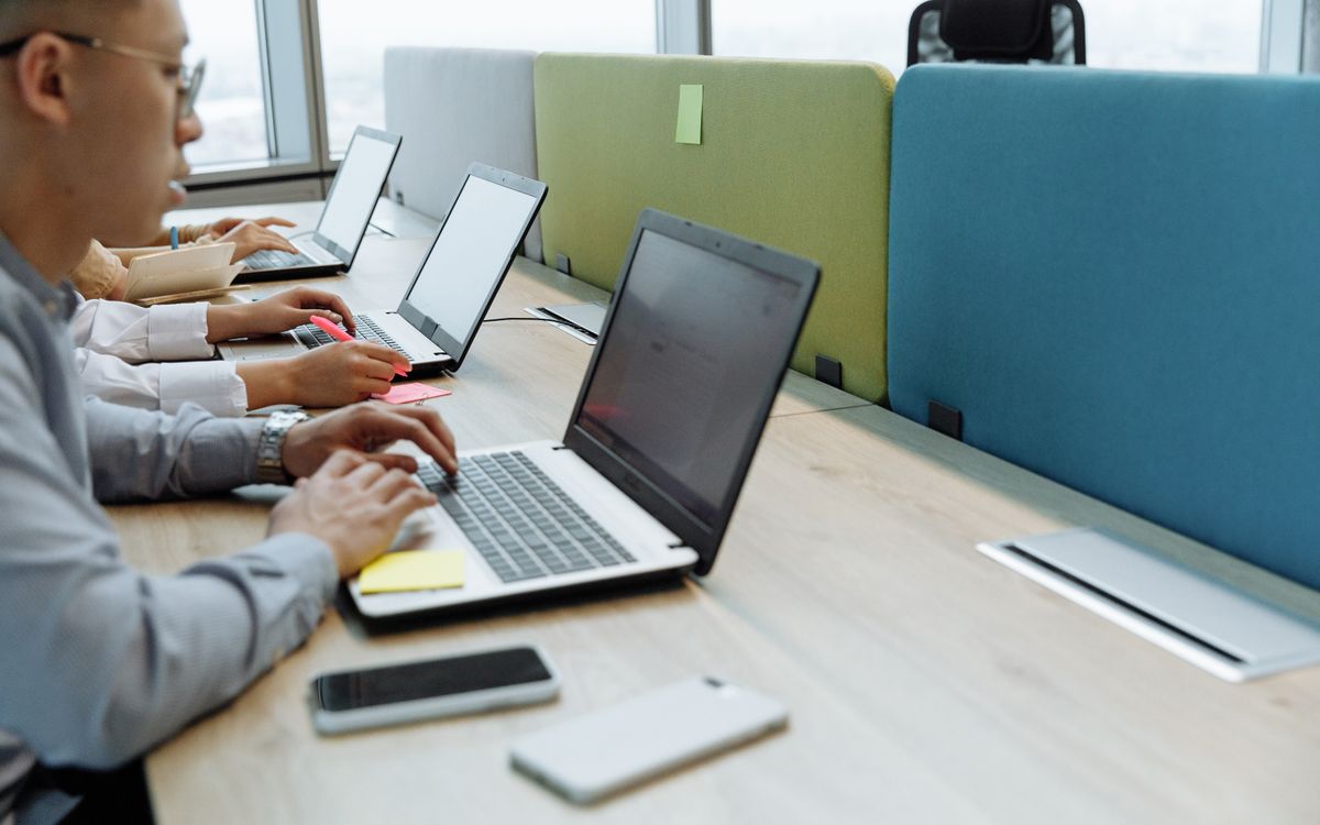 Colleagues working diligently at shared desks with laptops in a modern office space.