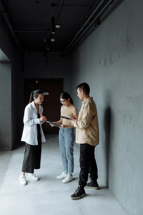 Free Three young professionals engaged in a team discussion inside a modern office hallway. Stock Photo