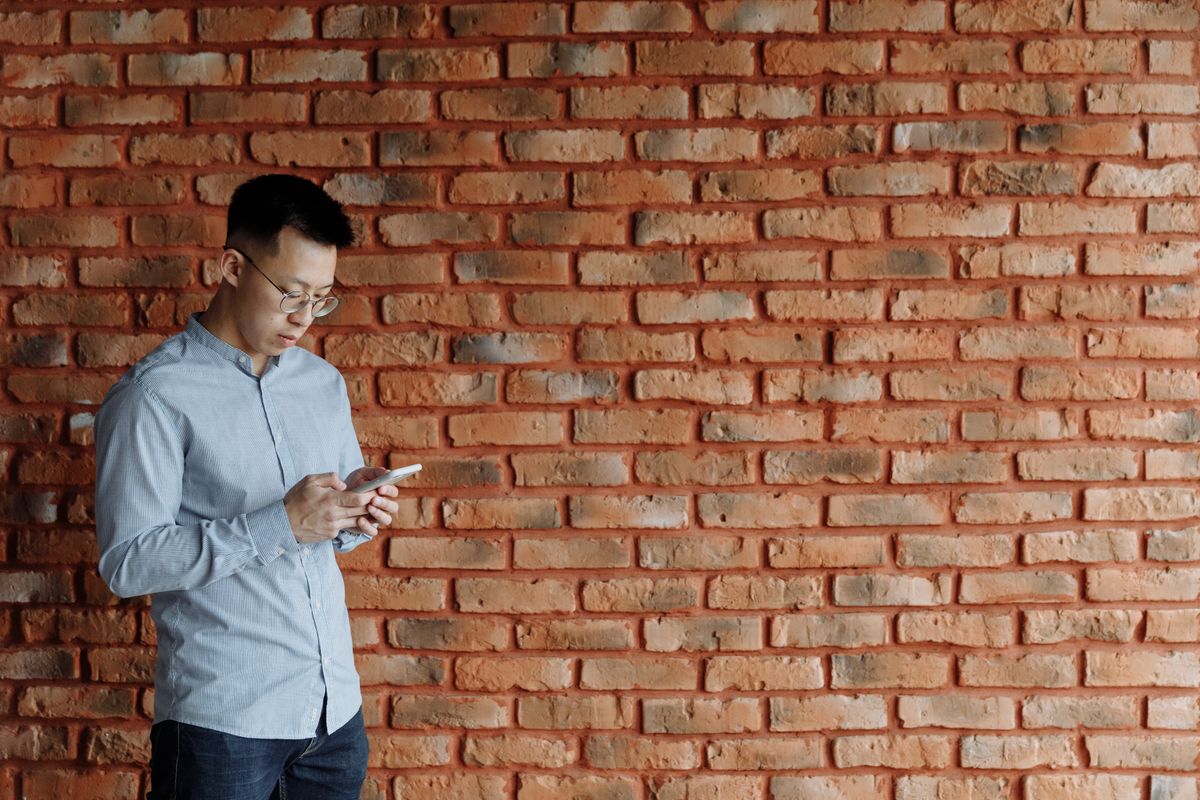 Man texting on a smartphone against a brick wall