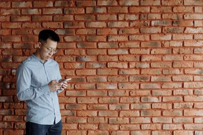 Man texting against a brick wall