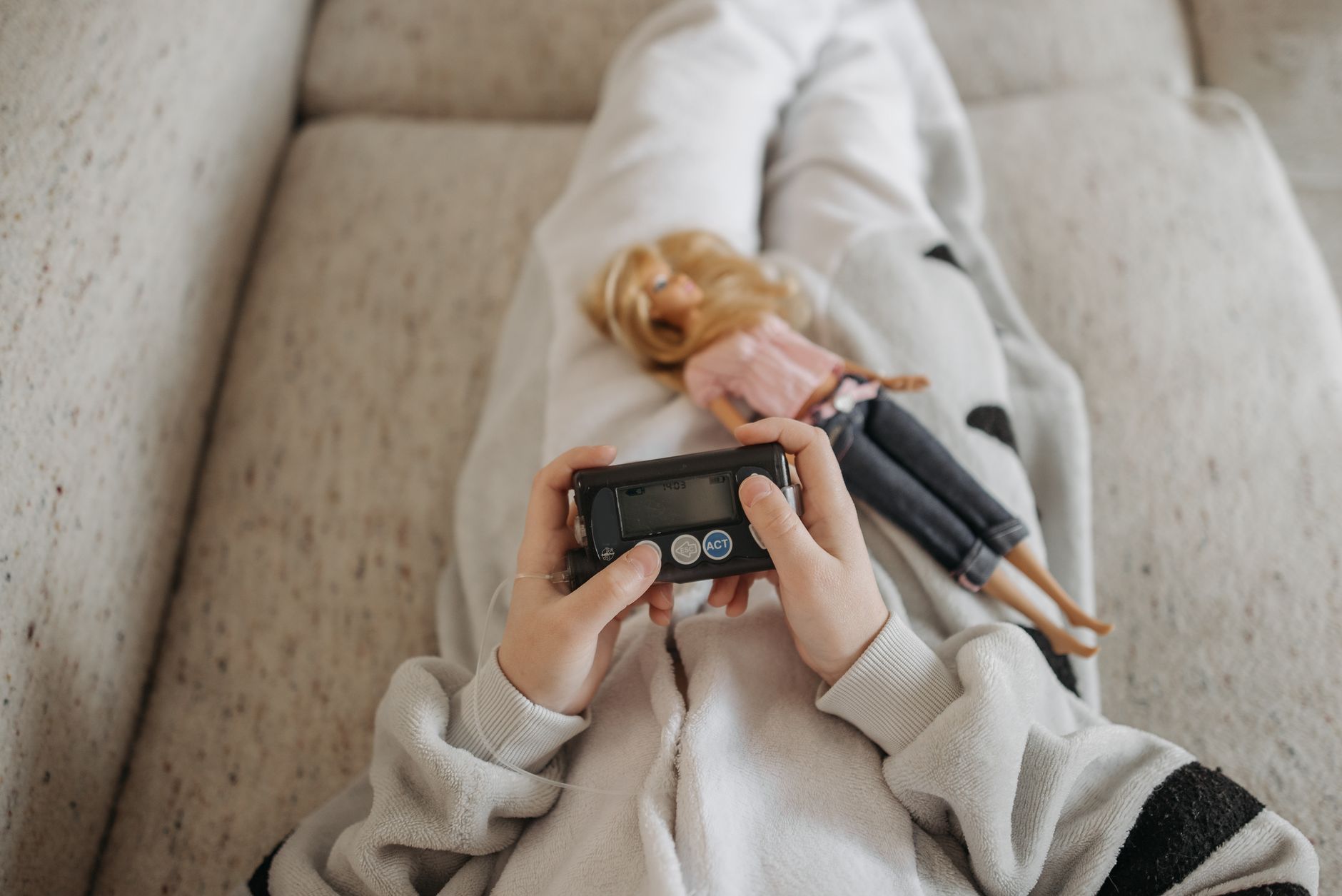 Close-up of a child holding an insulin pump with a doll resting on their lap, symbolizing diabetes management in daily life.