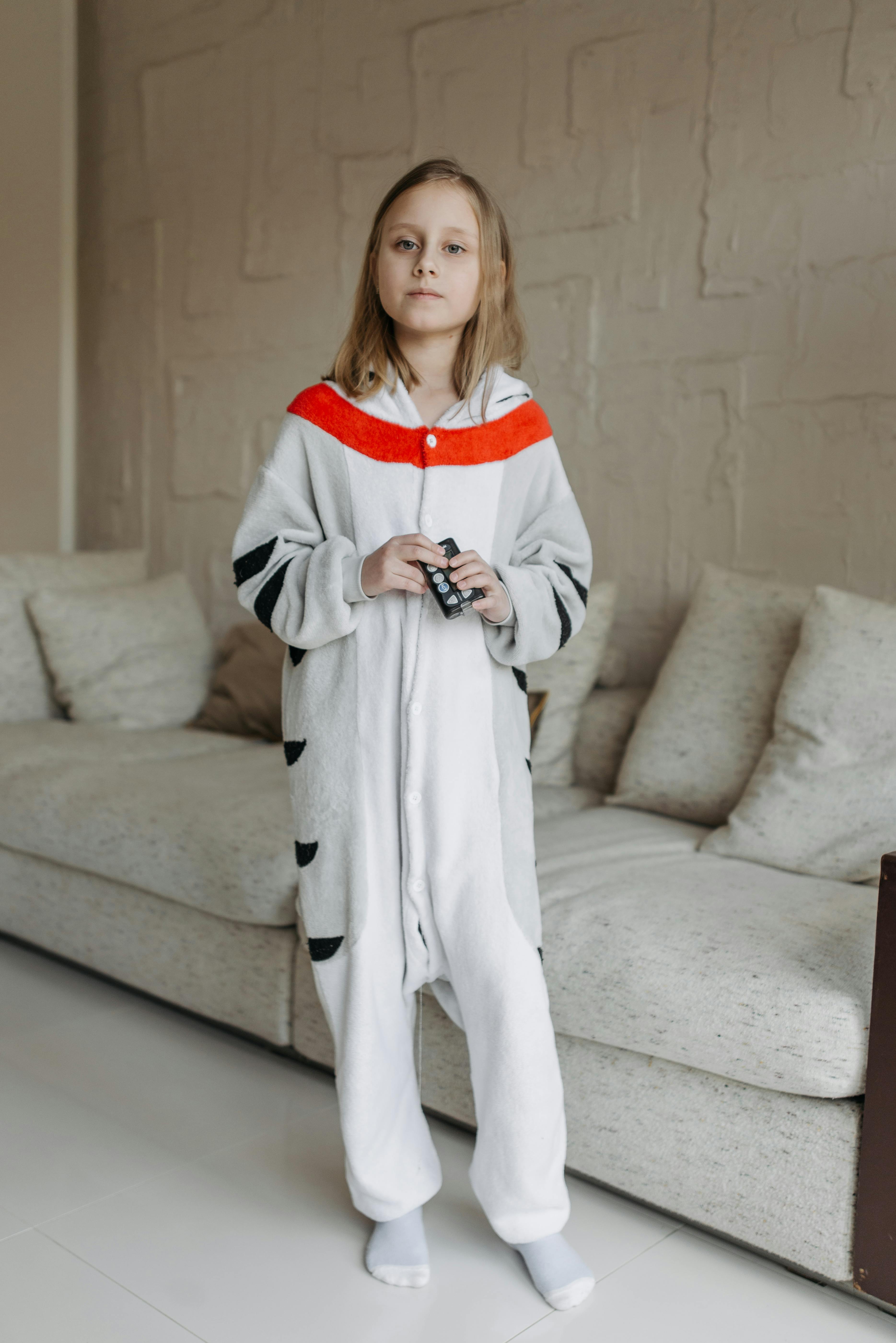 A young girl in a onesie at home, holding an insulin pump, showing diabetes management.