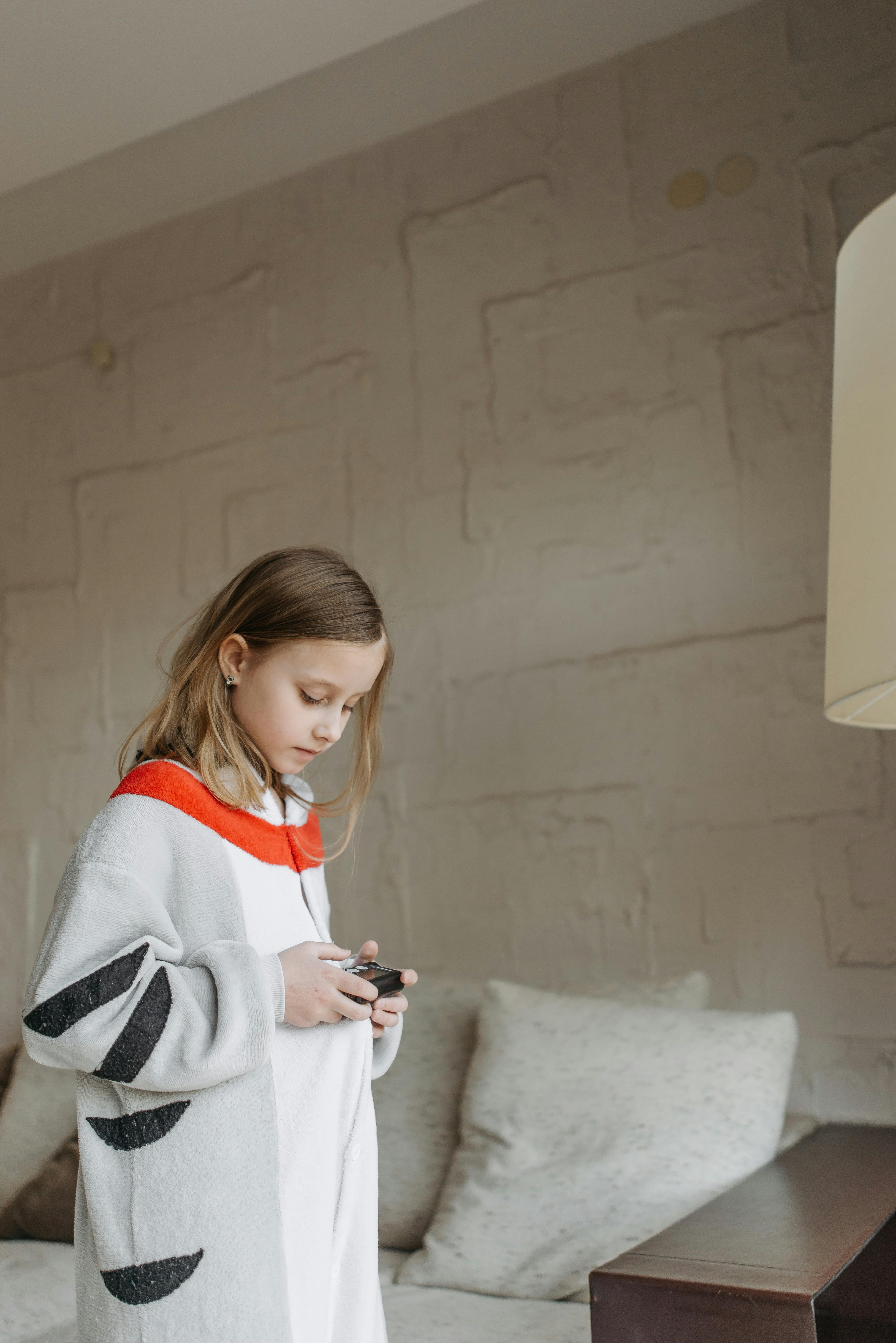 A young girl checks her insulin pump while wearing a comfortable onesie in a cozy room.