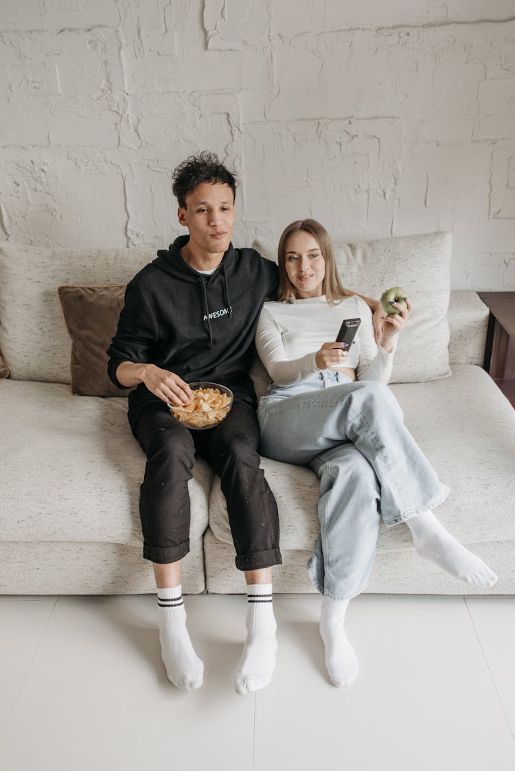 A Couple Sitting On A Couch While Watching Together