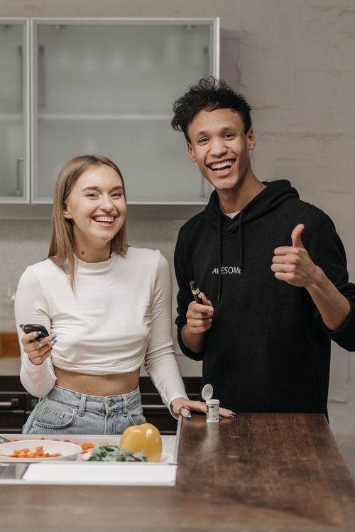 Free Smiling couple in kitchen holding glucometer and insulin pen, showing positivity in diabetes management. Stock Photo