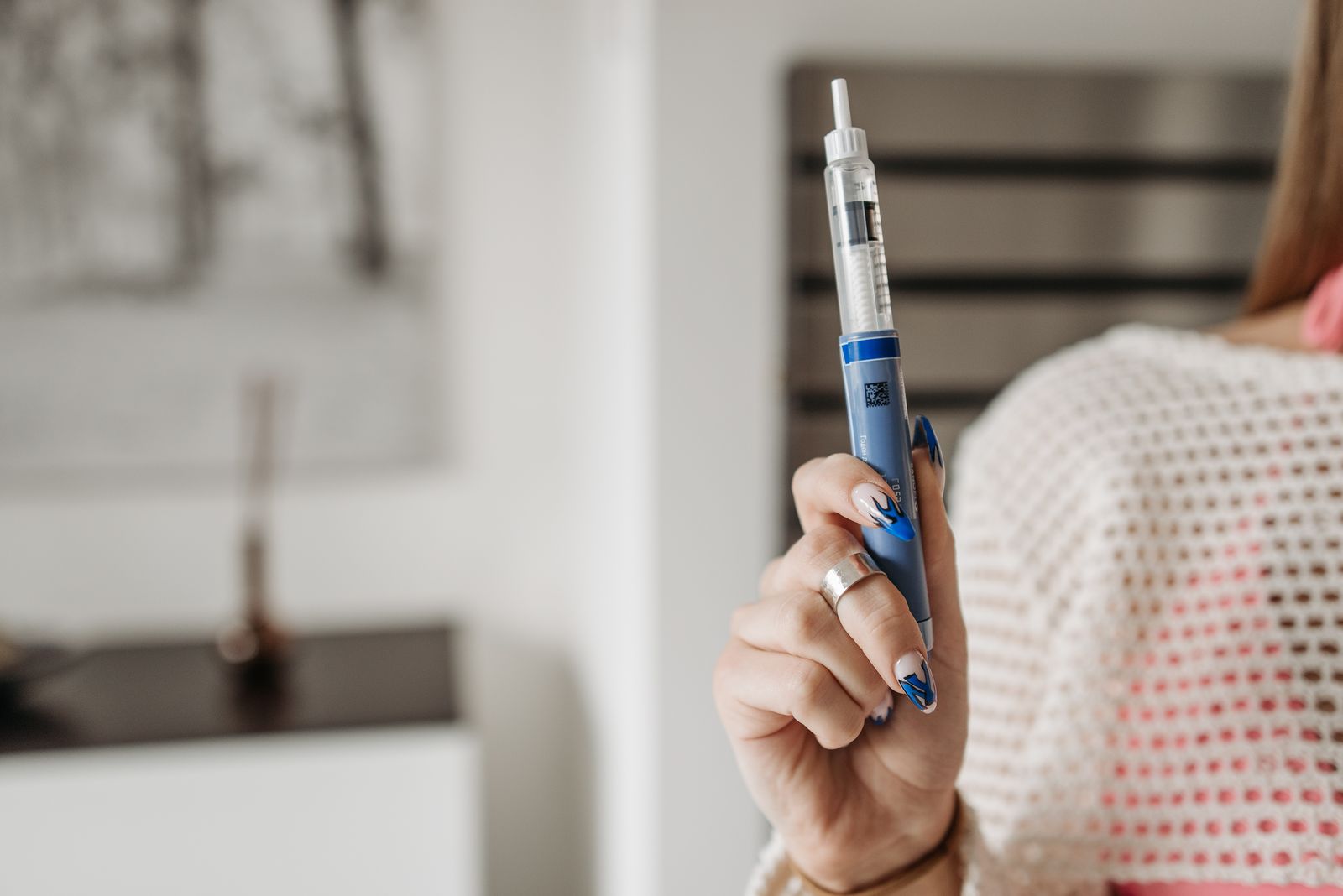 A woman at home holding an injection pen, the weekly ritual that most people abandon inside the first year